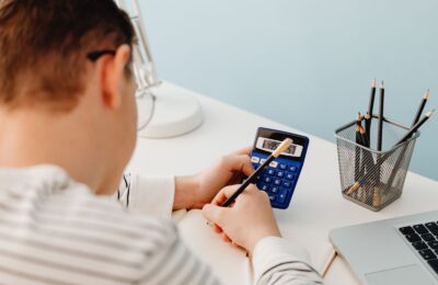 Estudiante hace cuentas con una calculadora junto a su laptop