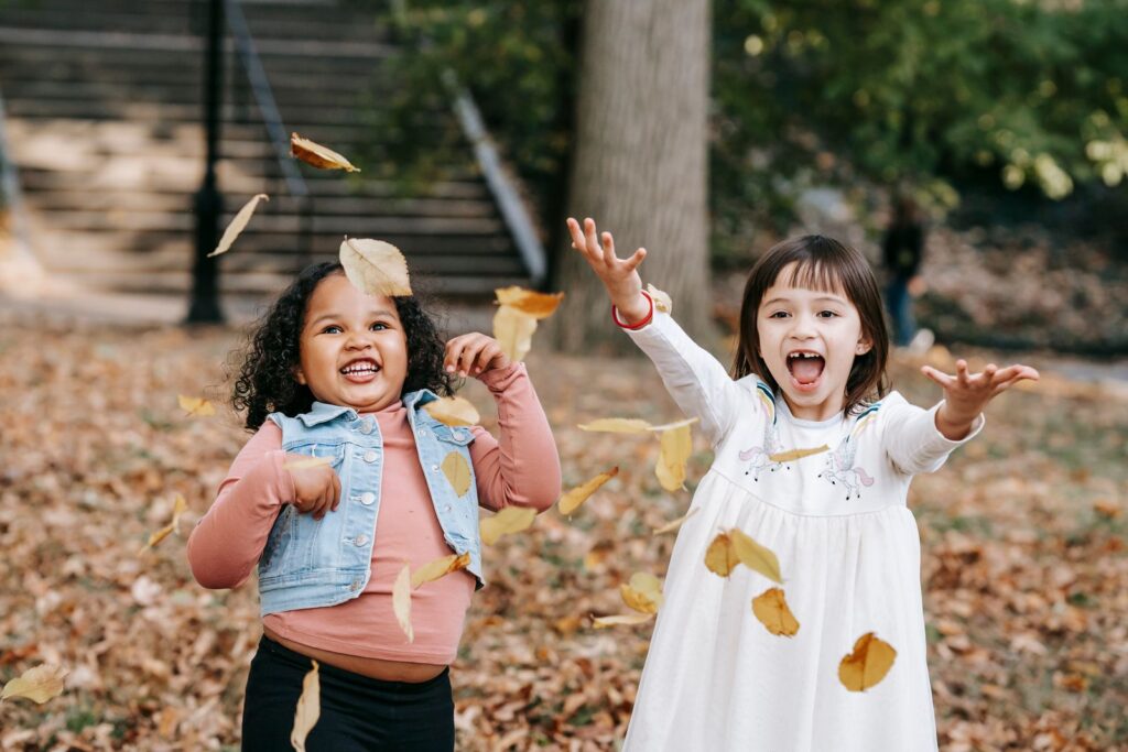 Dos niñas felices lanzan hojas secas en un parque en otoño