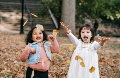 Dos niñas felices lanzan hojas secas en un parque en otoño